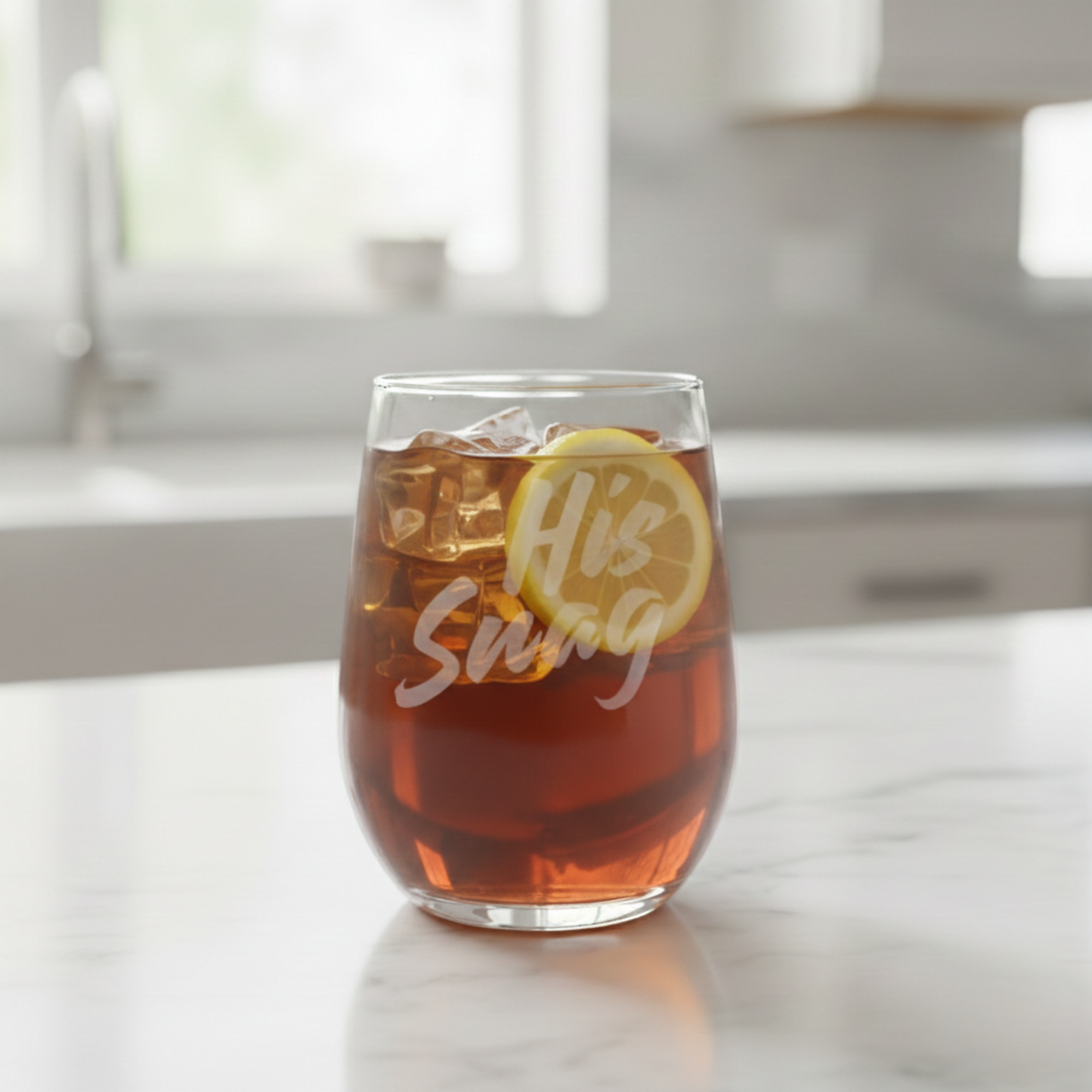 "His Snag" 20.5oz etched stemless wine glass by Expressive DeZien filled with iced tea and a lemon slice on a kitchen counter.