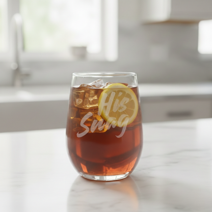 "His Snag" 20.5oz etched stemless wine glass by Expressive DeZien filled with iced tea and a lemon slice on a kitchen counter.