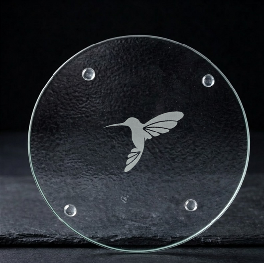 Clear glass trivet with a hummingbird design on a black background
