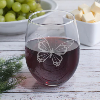 Wine glass with butterfly design on a wooden table with grapes and cheese.
